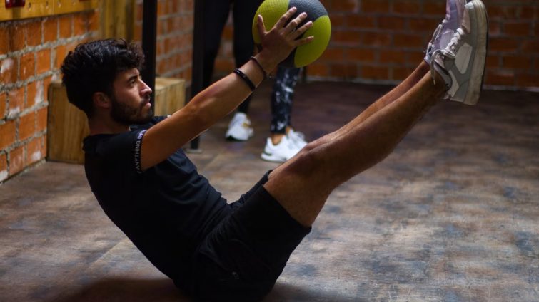 Focused man performing core exercises with a medicine ball in an indoor gym highlighting fitness and strength.